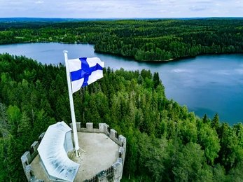 Finnish flag flying on a stone tower above a forest and lake
