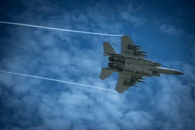 Jet fighter flying through a cloudy blue sky leaving vapor trails