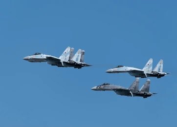 Silhouettes of three fighter jets flying above clouds at sunrise