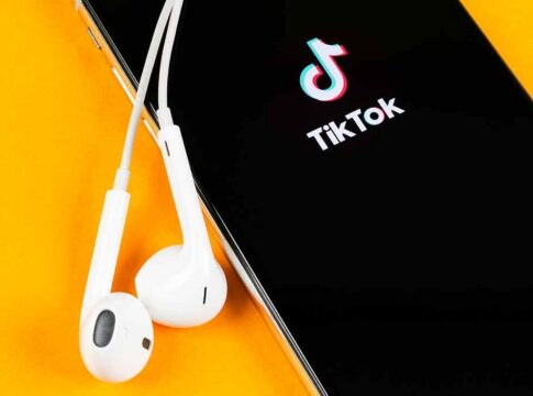 Smartphone with TikTok app and white wired earbuds on yellow background