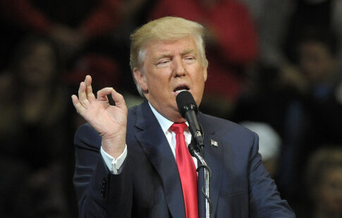 A man speaking into a microphone with a hand gesture during a speech
