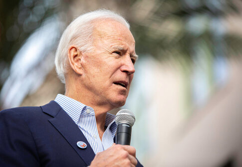 A man in a suit speaking into a microphone at an outdoor event
