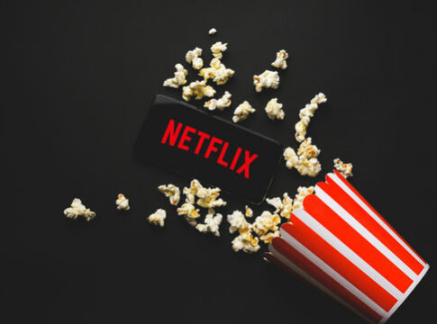 Spilled popcorn, phone displaying Netflix logo, striped popcorn container.