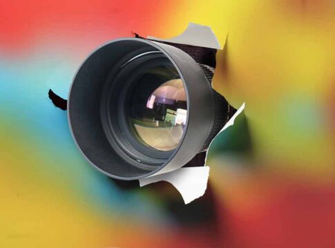 Camera lens emerging through torn paper
