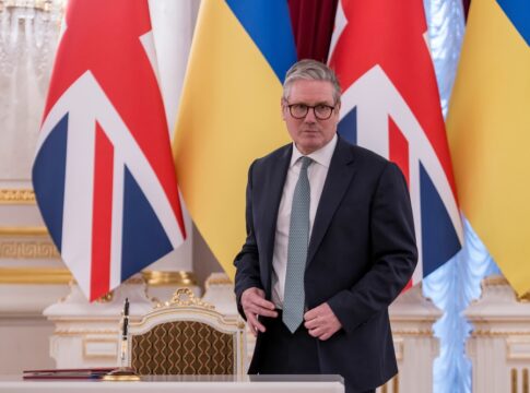 Man in suit stands before UK and Ukraine flags at a signing table